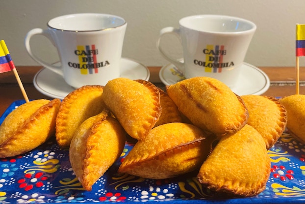 Several Chowe brand empanadas are shown artfully arranged on a plate adorned with two toothpicks representing the Columbian flag. In the background are two coffee cups imprinted with "Cafe du Colombia."