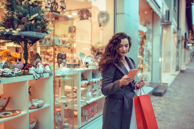 Woman doing her holiday shopping standing outside a store and looking at her phone.
