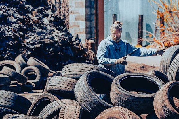 A man is pictured wearing gloves and picking up and sorting used tires for processing.