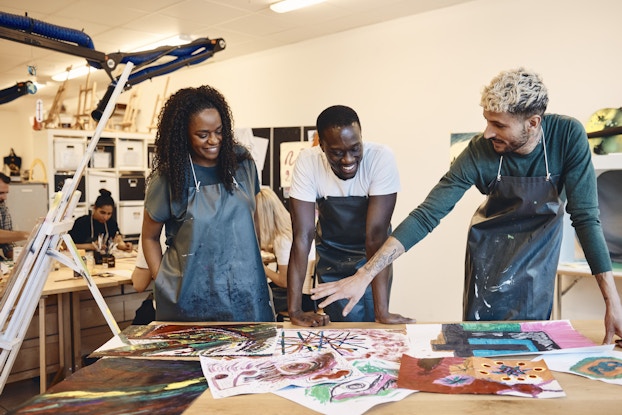 Group of people at an art studio looking at paintings on a table.