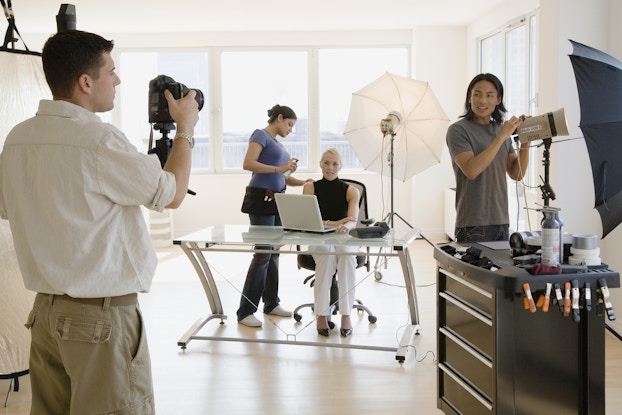 Photographers at an office taking photos of a corporate business woman behind a desk.