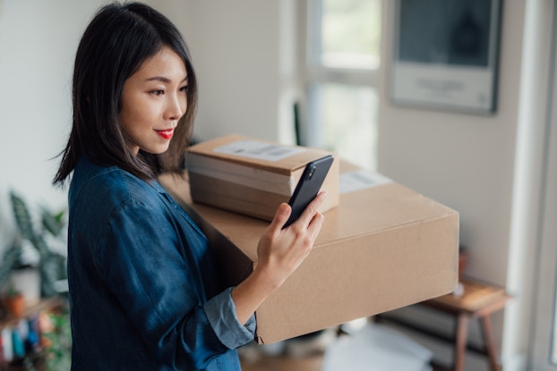 Woman packing up mailing boxes and looking at her phone.