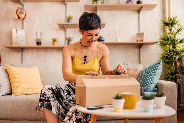 Woman happily unboxing a package inside her home.