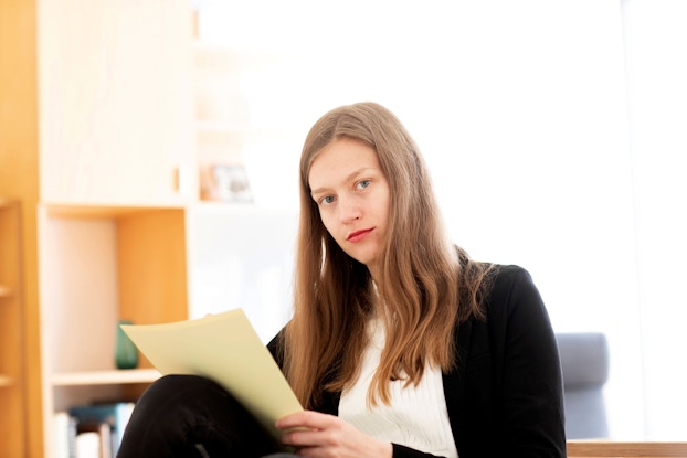 A young business woman looks at the viewer. She is holding papers in her hand and reviewing documents.