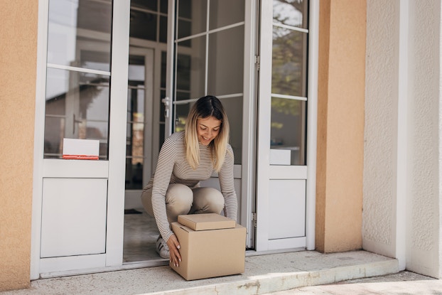 Woman bending down at her doorstep retrieving boxes.