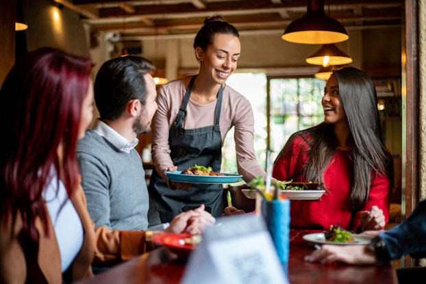Happy server handing plates to restaurant customers.
