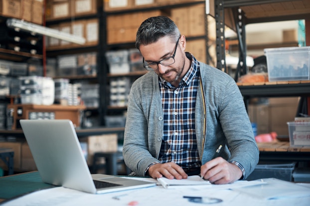 Business owner working in his warehouse on his laptop.