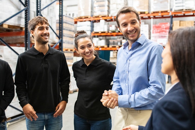 Group of employees in a warehouse standing together for a meeting.