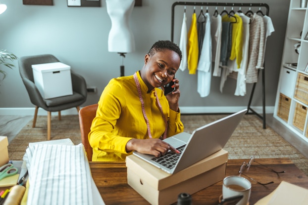 Smiling woman working on her laptop and talking on her phone.