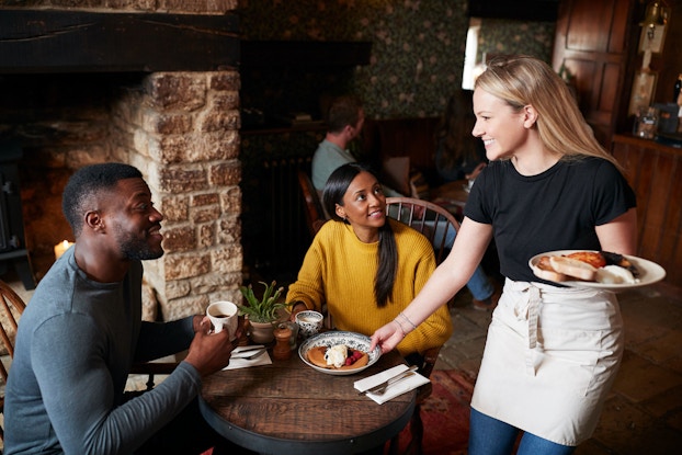 A waitress serves breakfast to two guests who are staying at a bed and breakfast.