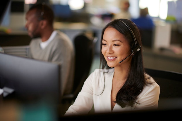 A woman employee of an offshore information technology vendor speaks with a client on the phone. She is wearing a headset and looking at a computer while she resolves a customer's problem.