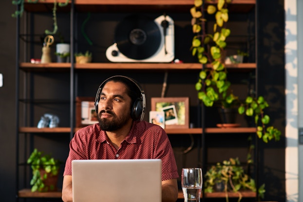 Man in his home office sitting at his desk listening to headphones.