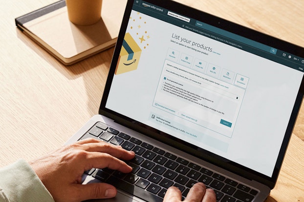 A pair of hands rest on the keyboard of an open laptop, the screen of which shows an Amazon seller page with the heading "List your products."