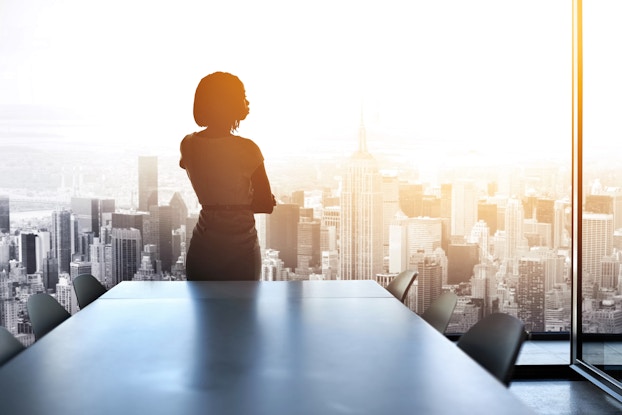 Professional woman standing in a conference room looking out on to the city through the floor-to-ceiling windows.