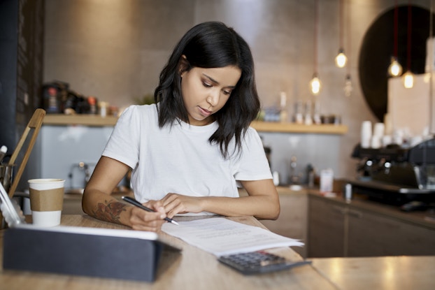 Woman business owner completes paperwork behind the register of her shop.