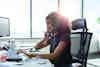 A woman is pictured sitting at a desk talking on the phone and typing on a keyboard.